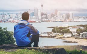 Young man at looking Auckland city skyline of city center and Auckland Sky Tower in New Zealand.