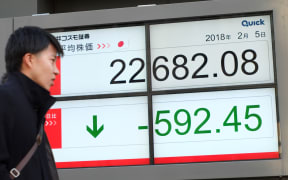 A pedestrian walks past an electronics stock indicator showing the closing numbers on the Tokyo Stock Exchange in Tokyo on February 5, 2018.