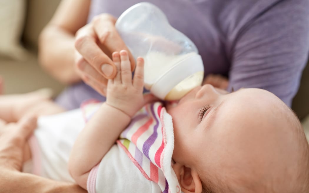 family, parenthood and people concept - close up of father feeding little daughter with baby formula from bottle at home
