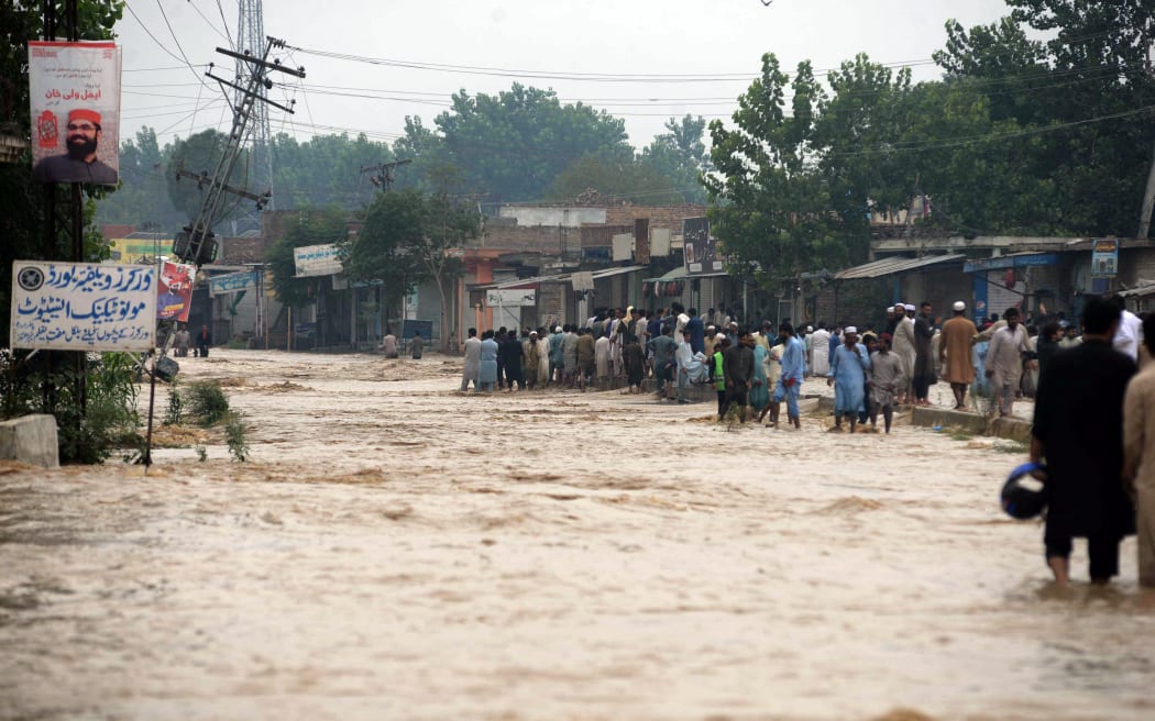 Pakistani people wade through flood water after flash floods hit the Charsadda district in northwest Khyber Pakhtunkhwa province, Pakistan on 28 August, 2022. Pakistan has called for international assistance and help in dealing with the floods that have killed more than 900 people since June.