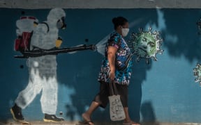 A woman walks past graffiti in Rio de Janeiro depicting a man performing a disinfection and the face of President Jair Bolsonaro represented by a virus.