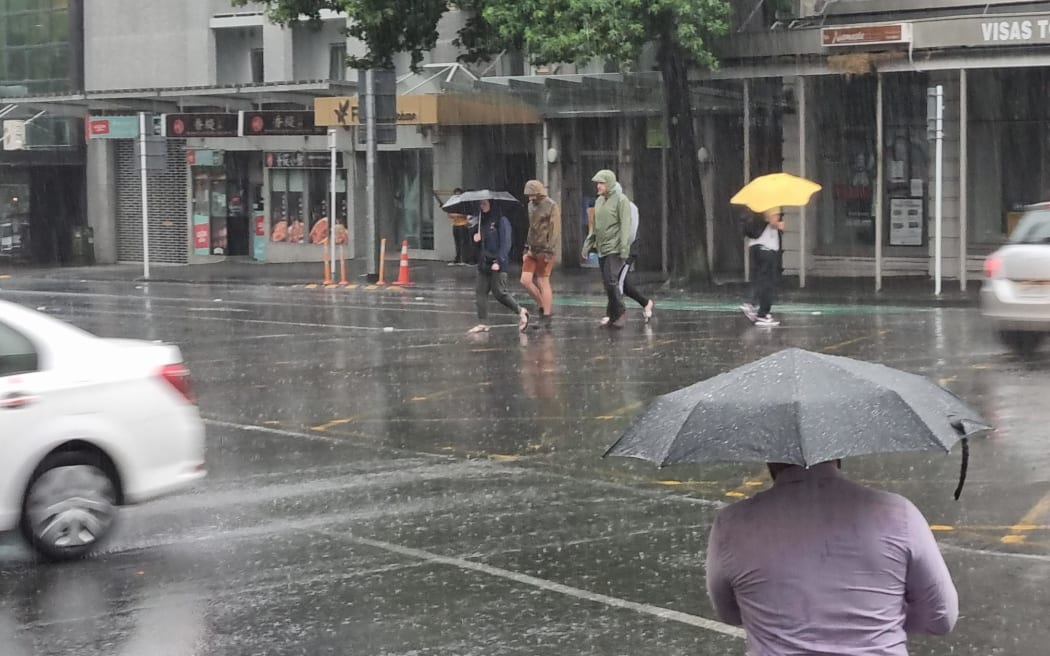 Pedestrians crossing the road during heavy rainfall in downtown Auckland.