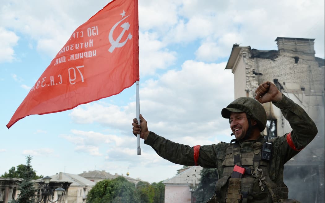 8228956 02.07.2022 A fighter of the 6th Platov Cossack Regiment of the LPR and a serviceman of the Chechen special police regiment named after Akhmat Kadyrov install the banner of the former Union of Soviet Socialist Republics, a symbol of victory in the Great Patriotic War, on the city administration building in Lisichansk, the Luhansk People's Republic. Viktor Antonyuk / Sputnik (Photo by Viktor Antonyuk / Sputnik / Sputnik via AFP)
