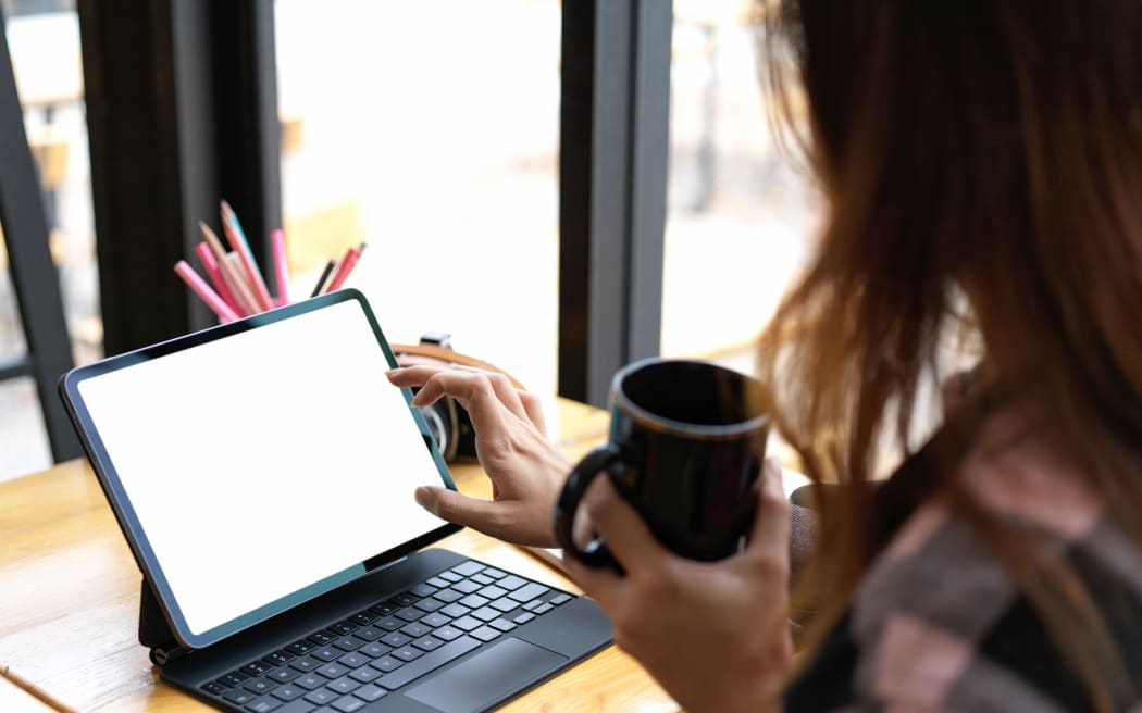 Cropped shot of female teenager holding cup and using digital tablet on wooden table in cafe, clipping path