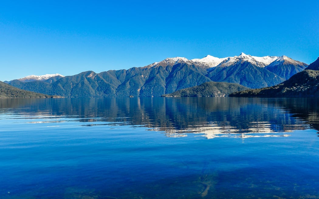 Reflection of snowy mountains in Lake Hauroko in the Southern Scenic Route, New Zealand