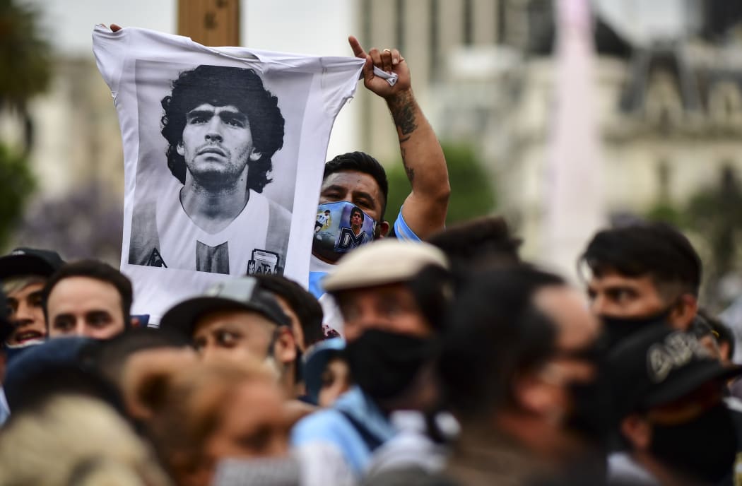 A man waves t-shirt with a picture of Diego Maradona as fans wait to enter Government House to pay tribute to the late football legend, Buenos Aires, 26 November.