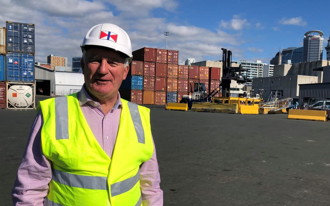 Brodie Stevens, in a hard hat and his-vis vest, standing at Ports of Auckland in front of a large number of shipping containers