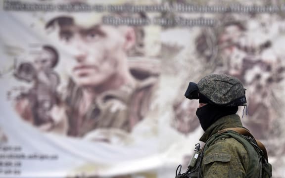 A Russian soldier in front of a Ukrainian army recruitment poster in Crimea.