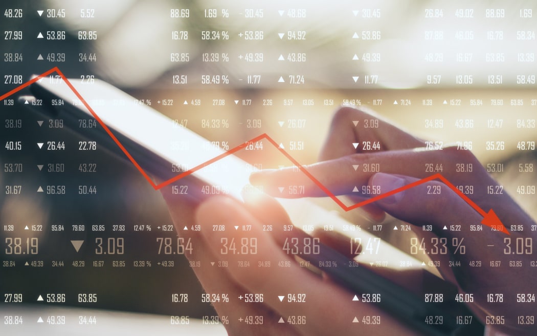 Close up of hand using tablet with financial digits and downward red arrow on blurry background, illustrating economic decline.