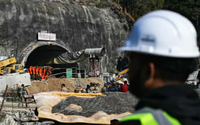 A rescue personnel stands near an entrance of the Silkyara under construction road tunnel, during the final phase of a rescue operation, days after a portion of it collapsed in the Uttarkashi district of India's Uttarakhand state on November 23, 2023. Ambulances were on standby on November 23 morning, as Indian rescuers dug through the final metres of debris separating them from 41 workers trapped in a collapsed road tunnel for nearly two weeks. (Photo by Arun SANKAR / AFP)
