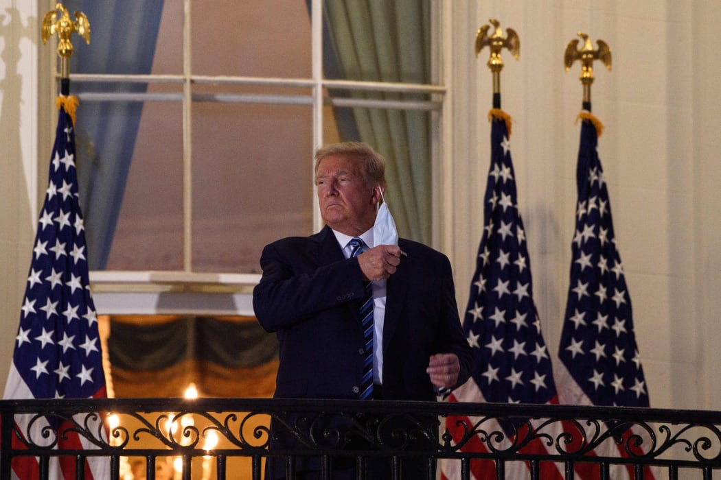 US President Donald Trump takes off his facemask as he arrives at the White House on 5 October, on his return from Walter Reed Medical Center, where he underwent treatment for Covid-19.