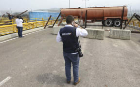 An immigration official observes a fuel tanker, cargo trailers and makeshift fencing, used as barricades by Venezuelan authorities trying to stop aid