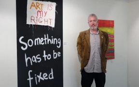 Leo stands beside artwork saying Art is My Right and Something has to be fixed