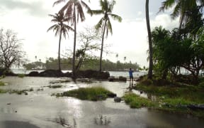 Atoll nations are seeing an increased frequency in ocean inundations during high tides and storms. In this 2016 file photo of Majuro Atoll in the Marshall Islands, a photographer stands ankle deep in water as ocean water floods over the island and onto the main road in the foreground.