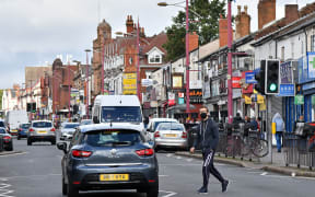 A man wearing a protective face mask crosses Soho Road in the Handsworth area of Birmingham, central England on August 22, 2020.