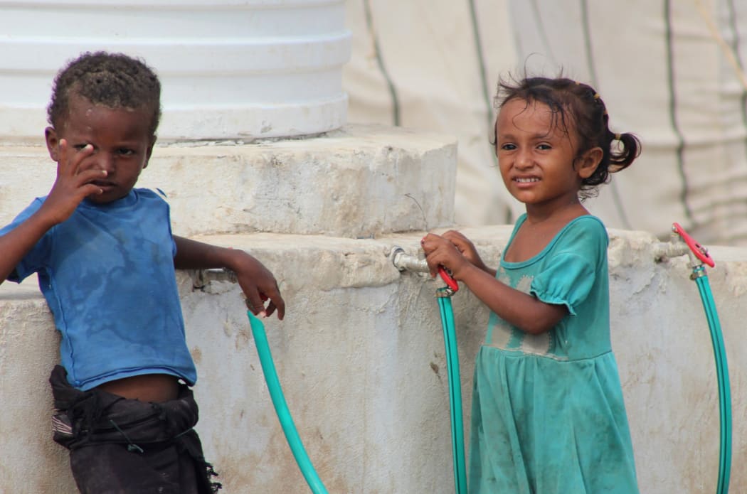 Displaced Yemeni children stand by a water storage tank in a camp set up for people who fled the battle areas east of the port city of Hodeida on September 15 2018.