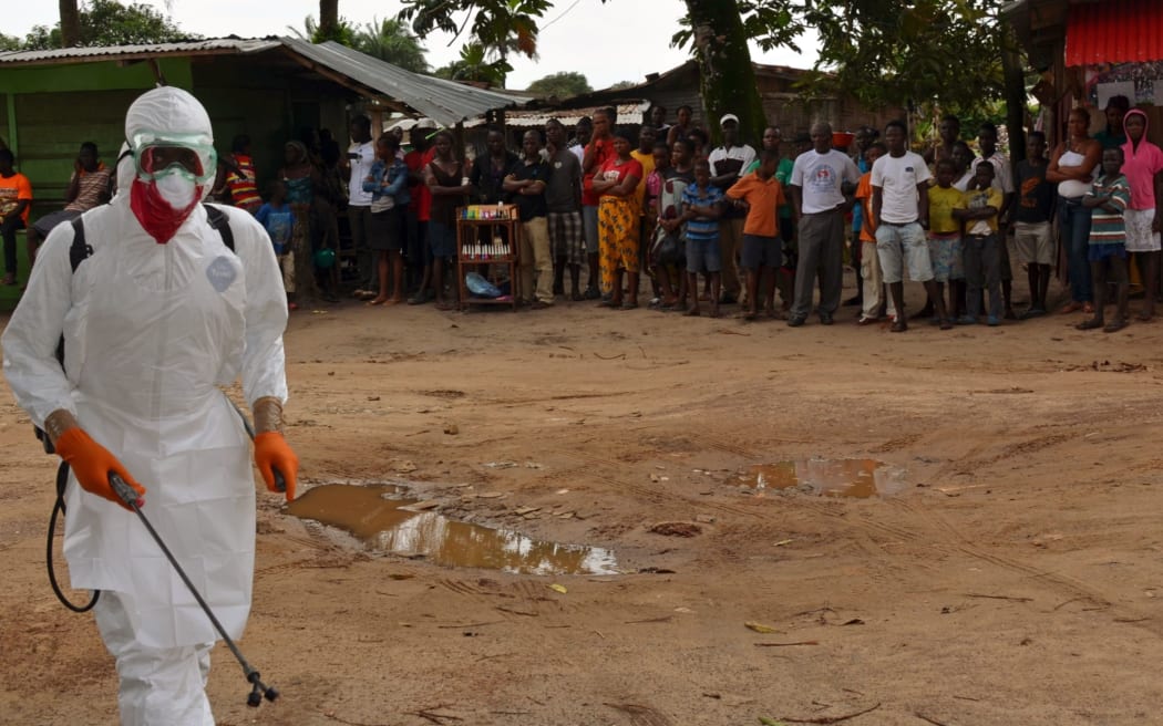 A Liberian Red Cross health worker  disinfects a courtyard  after the body of a victim of the Ebola virus was found.