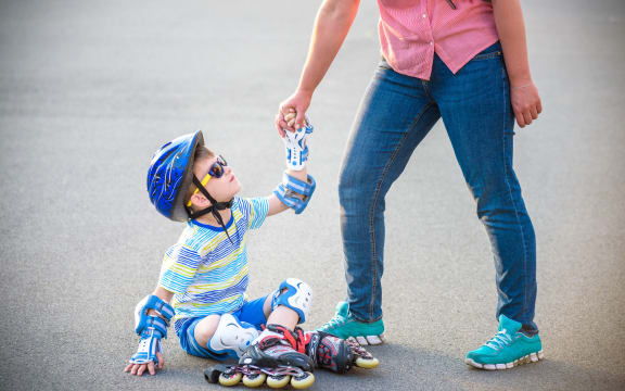 A photo of a Preschooler falling over while rollerblading with mother in the park.