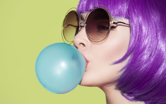 Pop art woman portrait wearing purple wig. Blow a blue bubble chewing gum. Olive background.