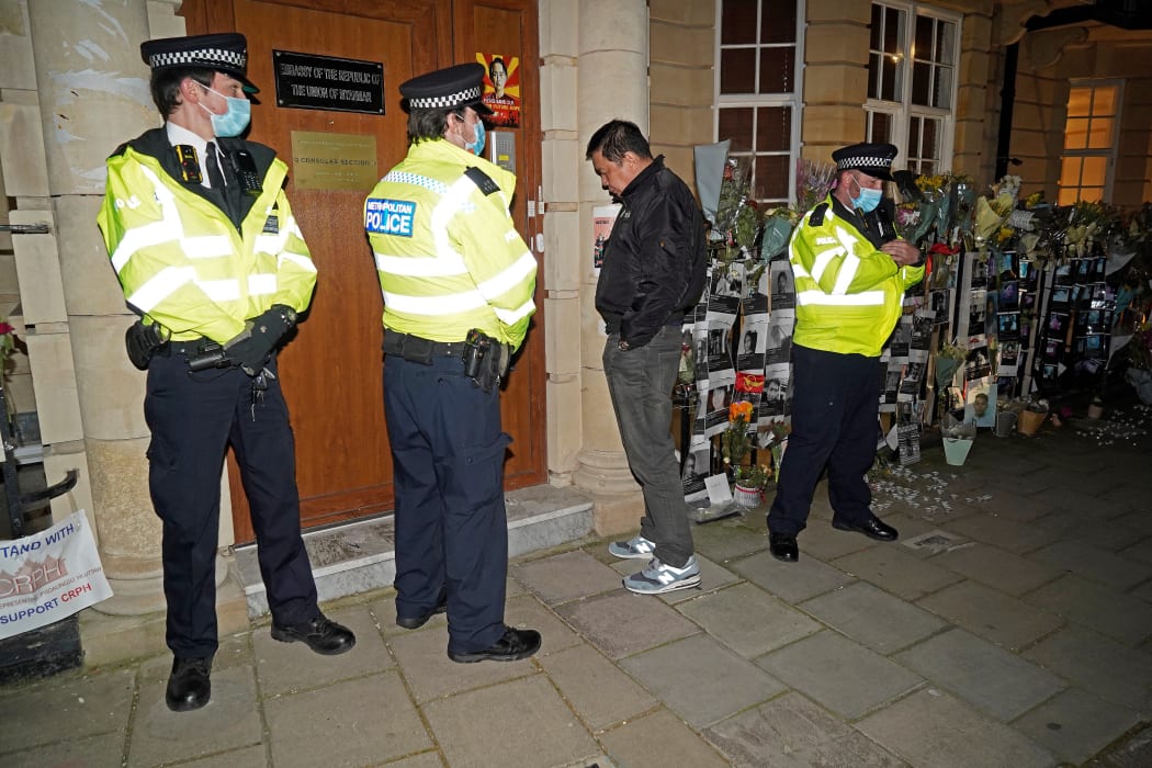 Myanmar's Ambassador to the United Kingdom, Kyaw Zwar Minn, waits unsuccessfully for an answer on the intercom, as police officers stand on duty outside the Myanmar Embassy in London on April 7, 2021.