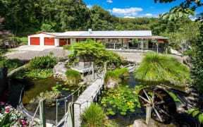 A house with a large pond and a waterwheel in front of it in Kawerau