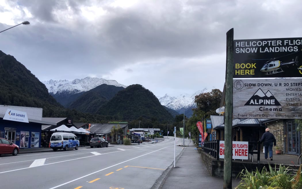 The main street of Franz Josef with snowy mountains in the background.