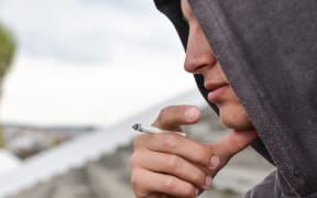A teenage boy wearing a hoodie smokes a cigarette.
