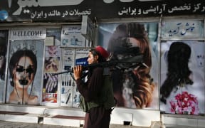 A Taliban fighter walks past a beauty salon with images of women defaced using spray paint in Shar-e-Naw in Kabul on 18 August 2021.