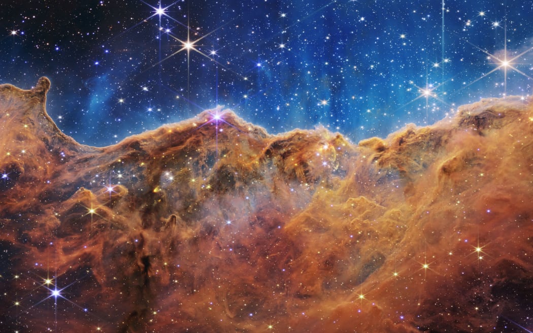 This image released by NASA on July 12, 2022, from the James Webb Space Telescope (JWST) shows a landscape of “mountains” and “valleys” speckled with glittering stars which is actually the edge of a nearby, young, star-forming region called NGC 3324 in the Carina Nebula. Captured in infrared light by the JWST, this image reveals for the first time previously invisible areas of star birth. - The JWST is the most powerful telescope launched into space and it reached its final orbit around the sun, approximately 930,000 miles from Earths orbit, in January, 2022. The technological improvements of the JWST and distance from the sun will allow scientists to see much deeper into our universe with greater detail. (Photo by Handout / NASA / AFP) / RESTRICTED TO EDITORIAL USE - MANDATORY CREDIT 