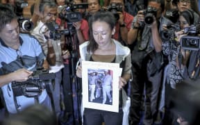 A relative of a passenger of flight MH370 holds a picture of Malaysian Prime Minister Najib Razak with the words "please bring back my husband".