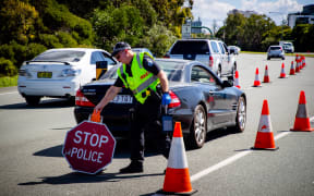 A Queensland police officer moves a stop sign at a vehicle checkpoint on the Pacific Highway, along the state's border with New South Wales, in Brisbane on April 15, 2020.