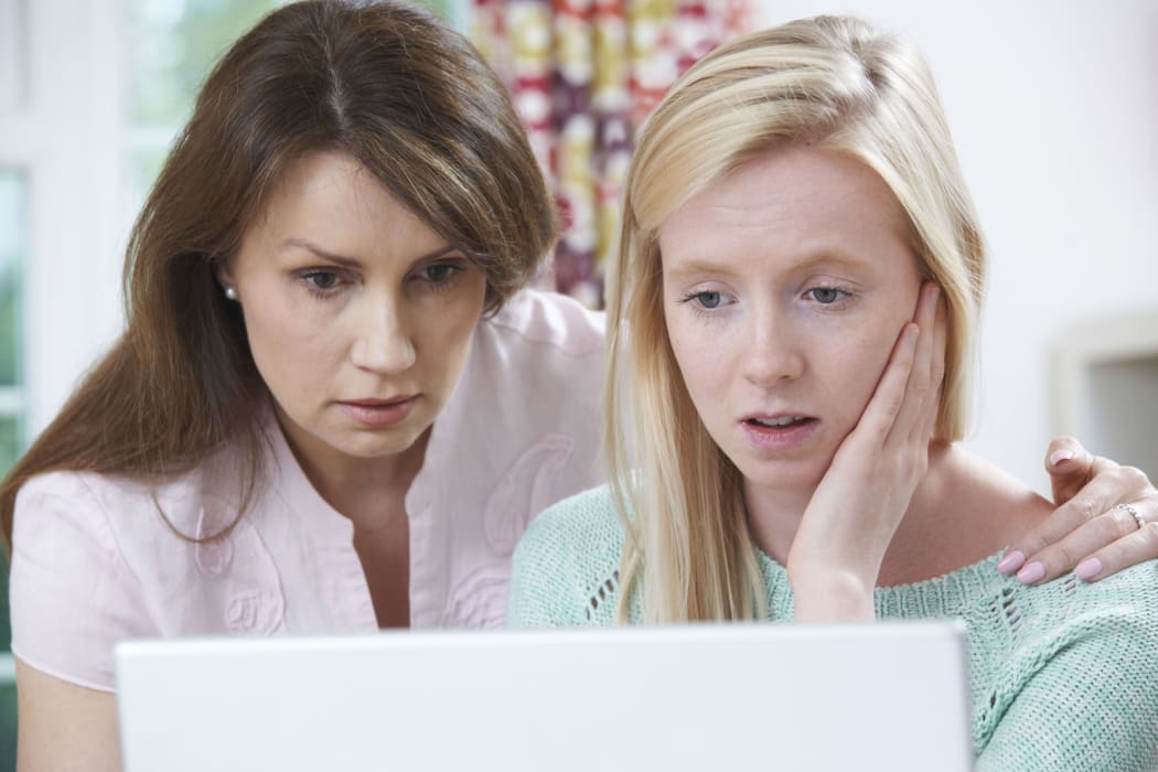 A photo of a concerned mother and daughter looking at a laptop