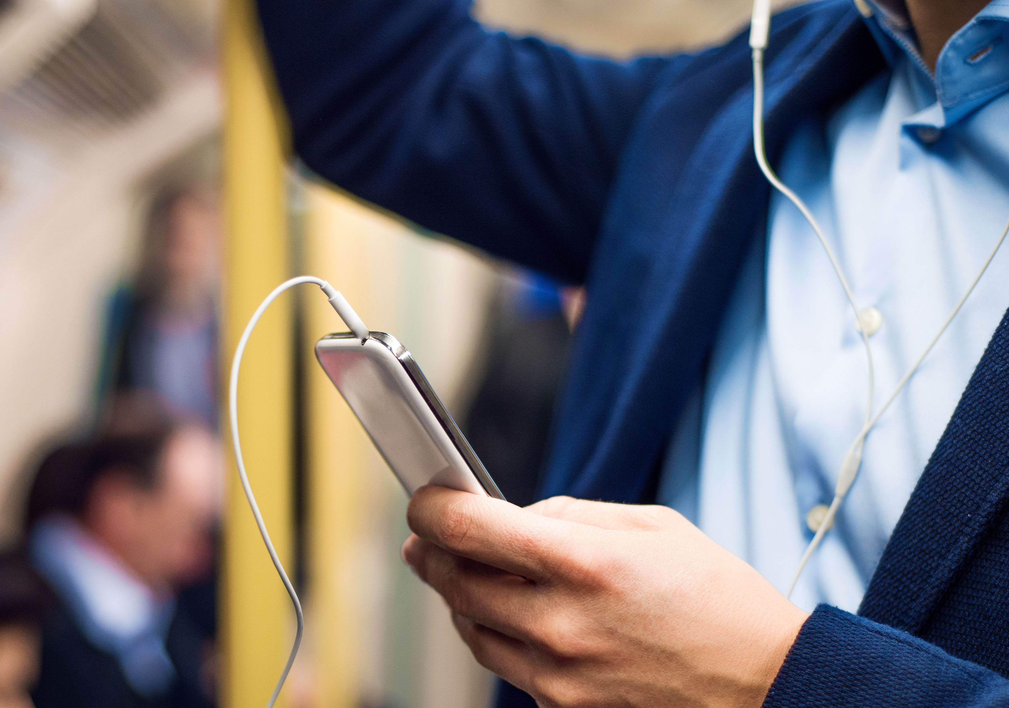 A man wearing headphones uses his smartphone on a train.