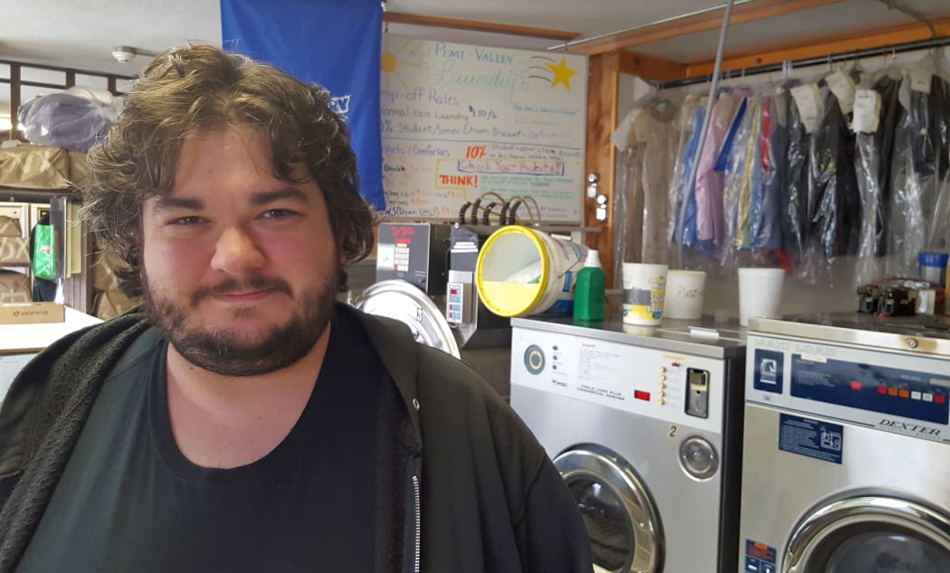 Bearded student stands in front of two big front loader washing machines