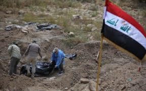 Members of the Iraqi security forces wearing protective clothes inspect a mass grave containing the remains of people believed to have been slain by jihadists of the Islamic State (IS) group at the Speicher camp