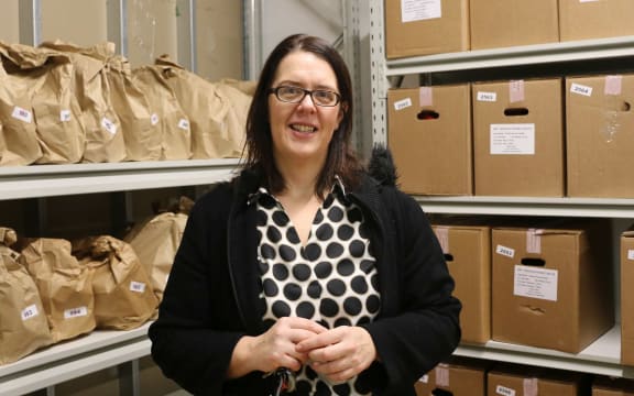 Woman stands in front of shelves with boxes and paper bags filled with food.