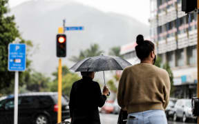 Whanarei, young and old woman stand at traffic lights, rain.
