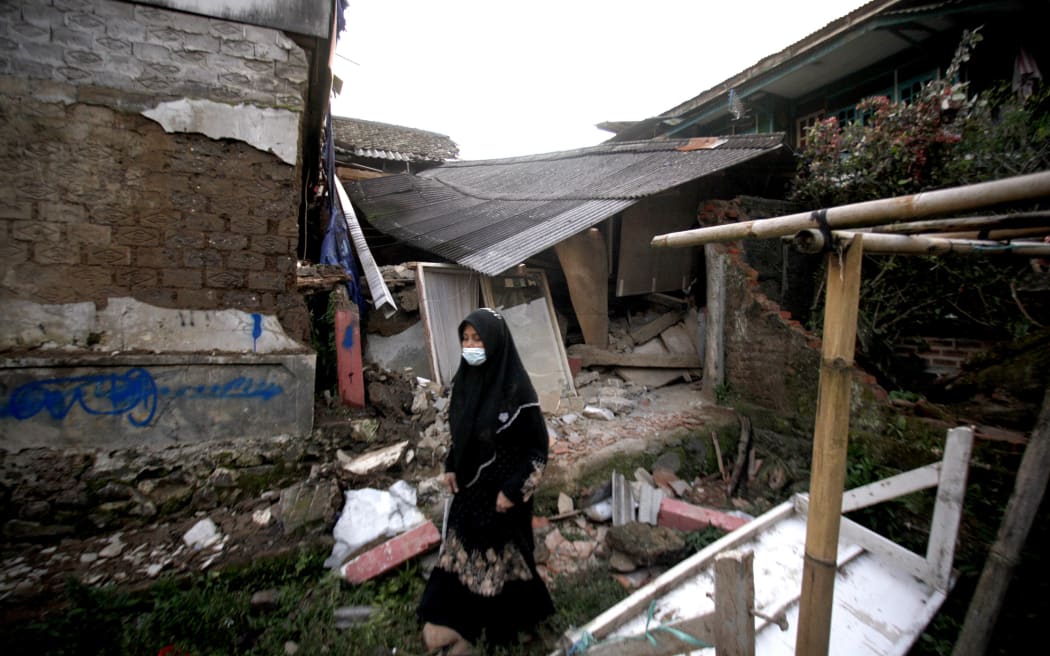 A woman walks past a damaged house following an earthquake in Cianjur on 21 November, 2022.