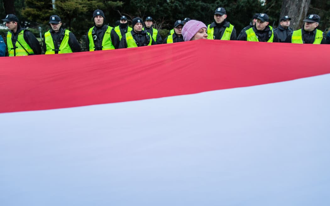 A woman holds a giant Polish national flag as People attend the anti-government demonstration of opposition parties supporters and Committee for the Defence of Democracy movement (KOD) the day after the parliament crisis in front of building of Polish Parliament, in Warsaw, on December 17