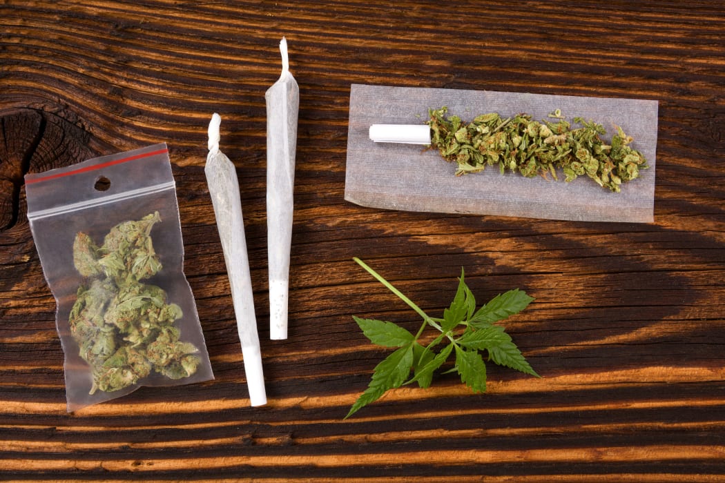 50549923 - marijuana background. cannabis joint, bud in plastic bag and hemp leaves on wooden table. addictive drug or alternative medicine.