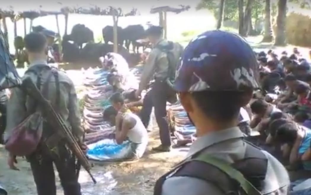 A screen capture of the footage which shows villagers sitting in lines in front of police officers.