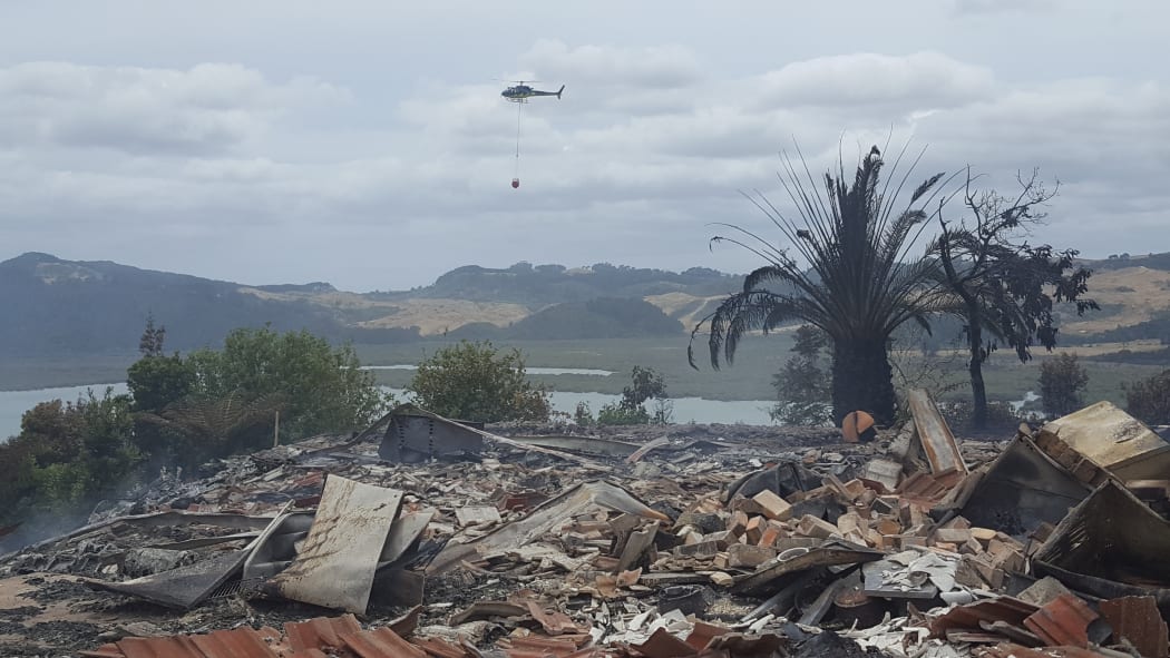 A monsoon helicopter flies over the remains of a house razed by a scrub fire near Whitianga. At least four houses and several other buildings have burnt to the ground.