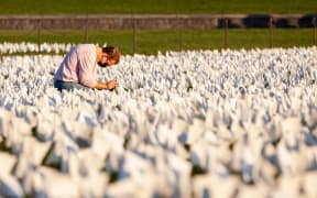 A person kneels to take photos of some of the more than 670,000 white flags covering 20 acres of the National Mall in an art memorial for Covid-19 victims by Suzanne Brennan Firstenberg In America: Remember.