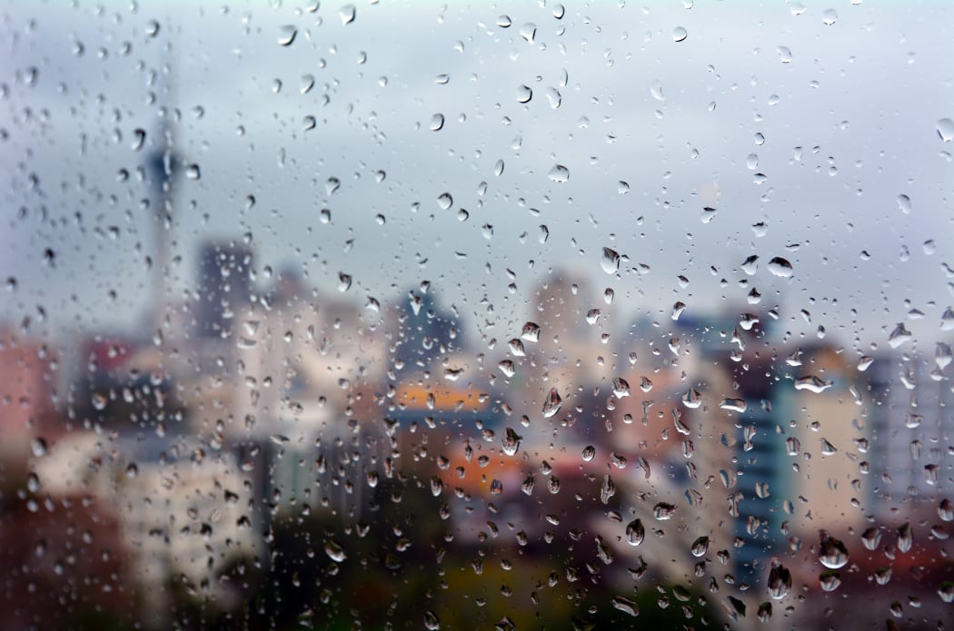 Urban view of rain drops falls on a window during a stormy day overlooking Auckland CBD New Zealand skyline in the background.