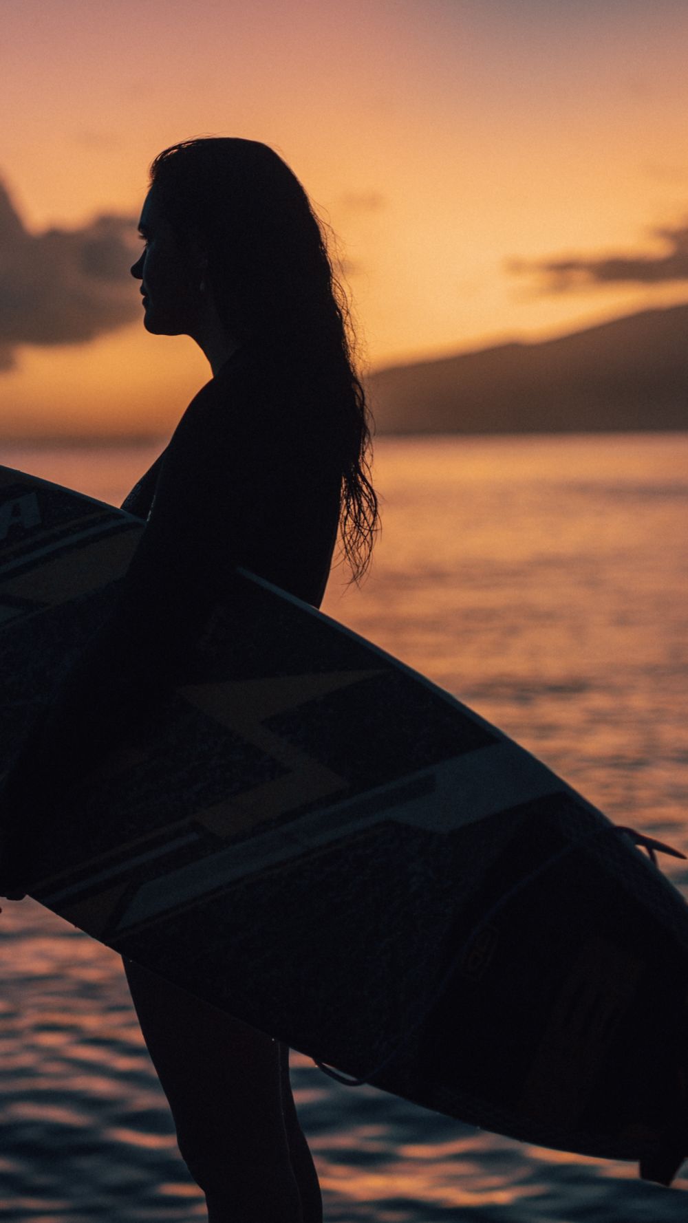 Zhana poses with her surfboard at sunset