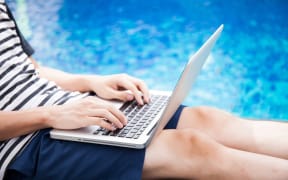 A man with a laptop checks his work emails by the pool (file).