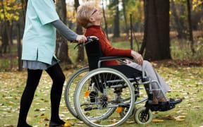 Disabled senior woman with young nurse walking at park