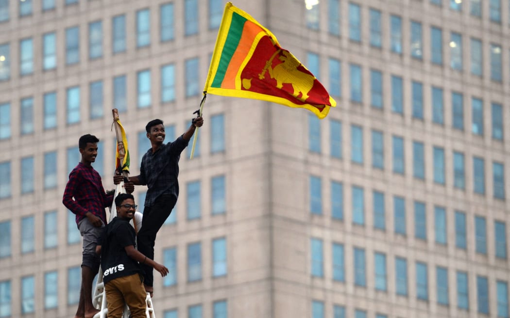 A man waves Sri Lanka's national flag after climbing a tower near presidential secretariat in Colombo on 1 July, 2022, after it was overrun by anti-government protesters.