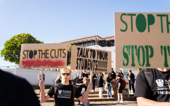 Massey University students hold signs that say 'stop the cuts' and 'talk to your students'.
