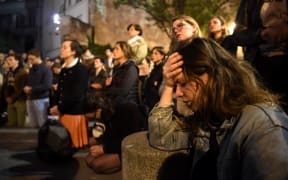 People kneel to pray on the pavement as flames engulf Notre-Dame Cathedral in Paris on April 15, 2019. - A